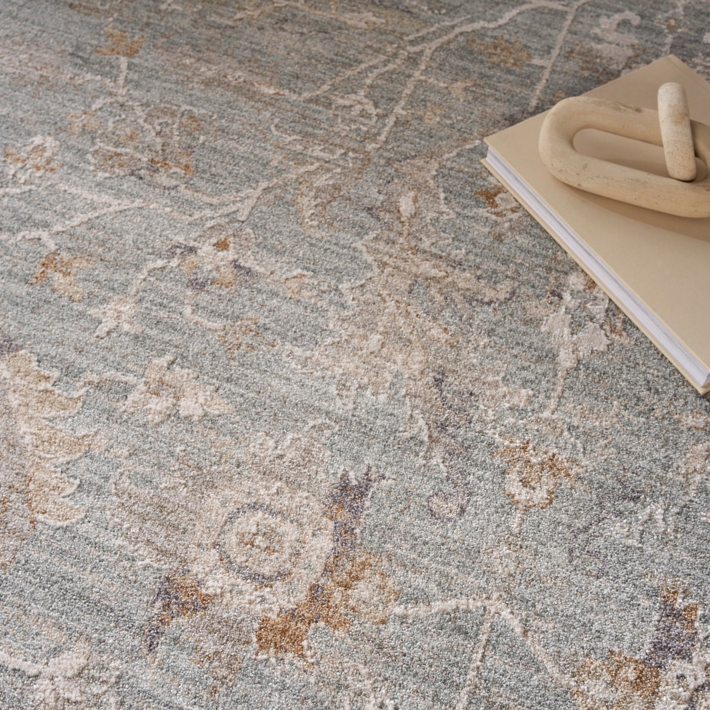 Blue-gray patterned rug with beige floral motifs; wooden doughnut-shaped accent sitting on a stacked notebook.