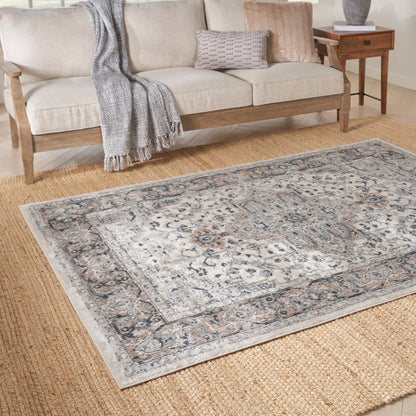 Neutral living room with beige sofa on wood frame, gray knit throw, and blue-gray oriental rug on natural jute floor.