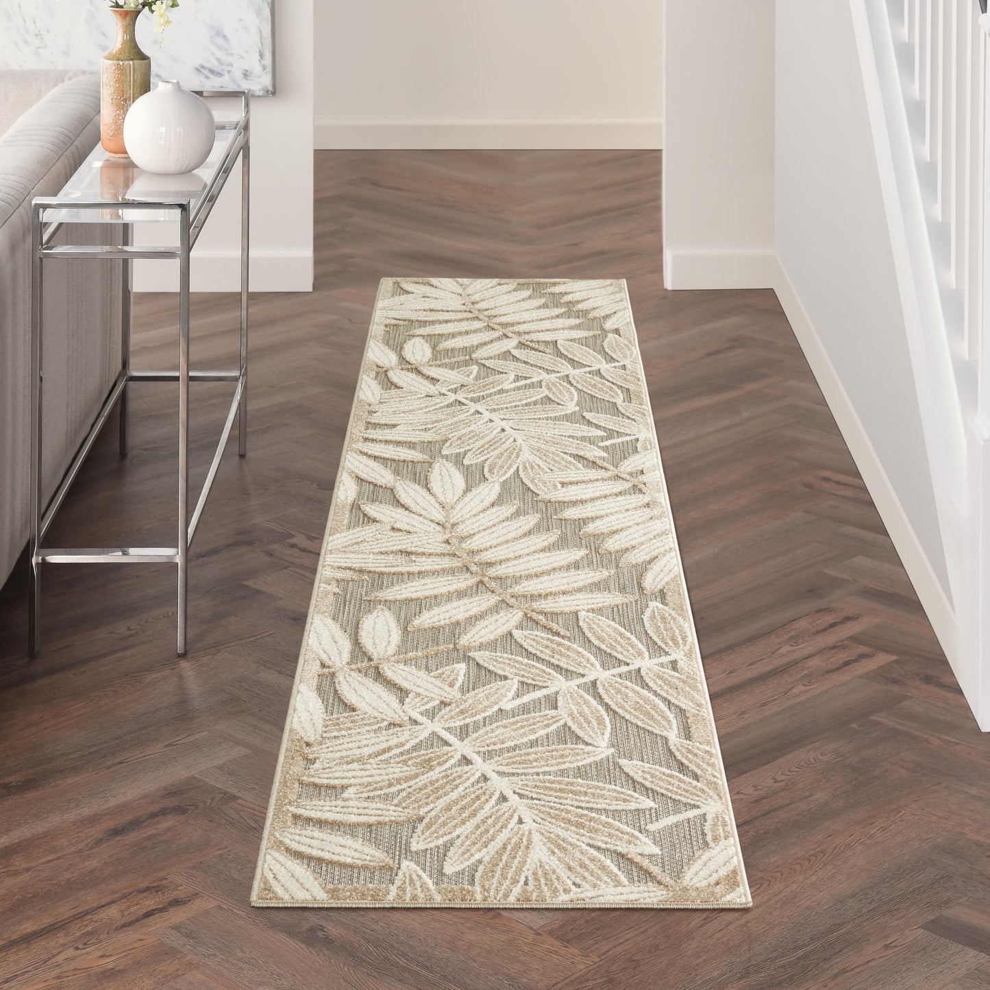 Beige cream botanical leaf runner rug on dark wood hallway floor beside a glass console.