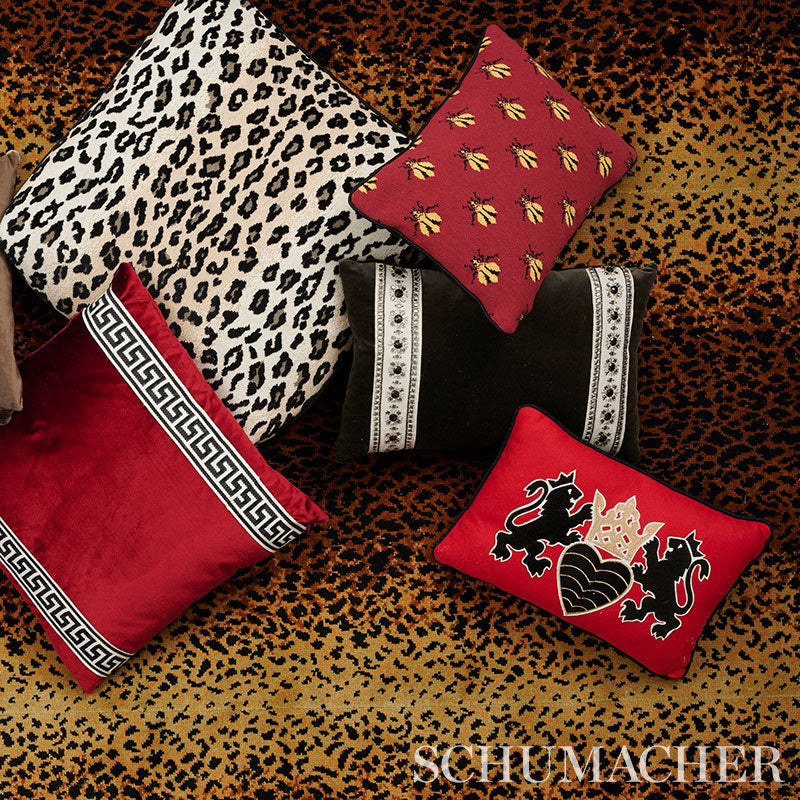Assorted decorative throw pillows on leopard-print fabric: red velvet with Greek key trim, bee motif, dragon crest, and leopard-pattern cushion.