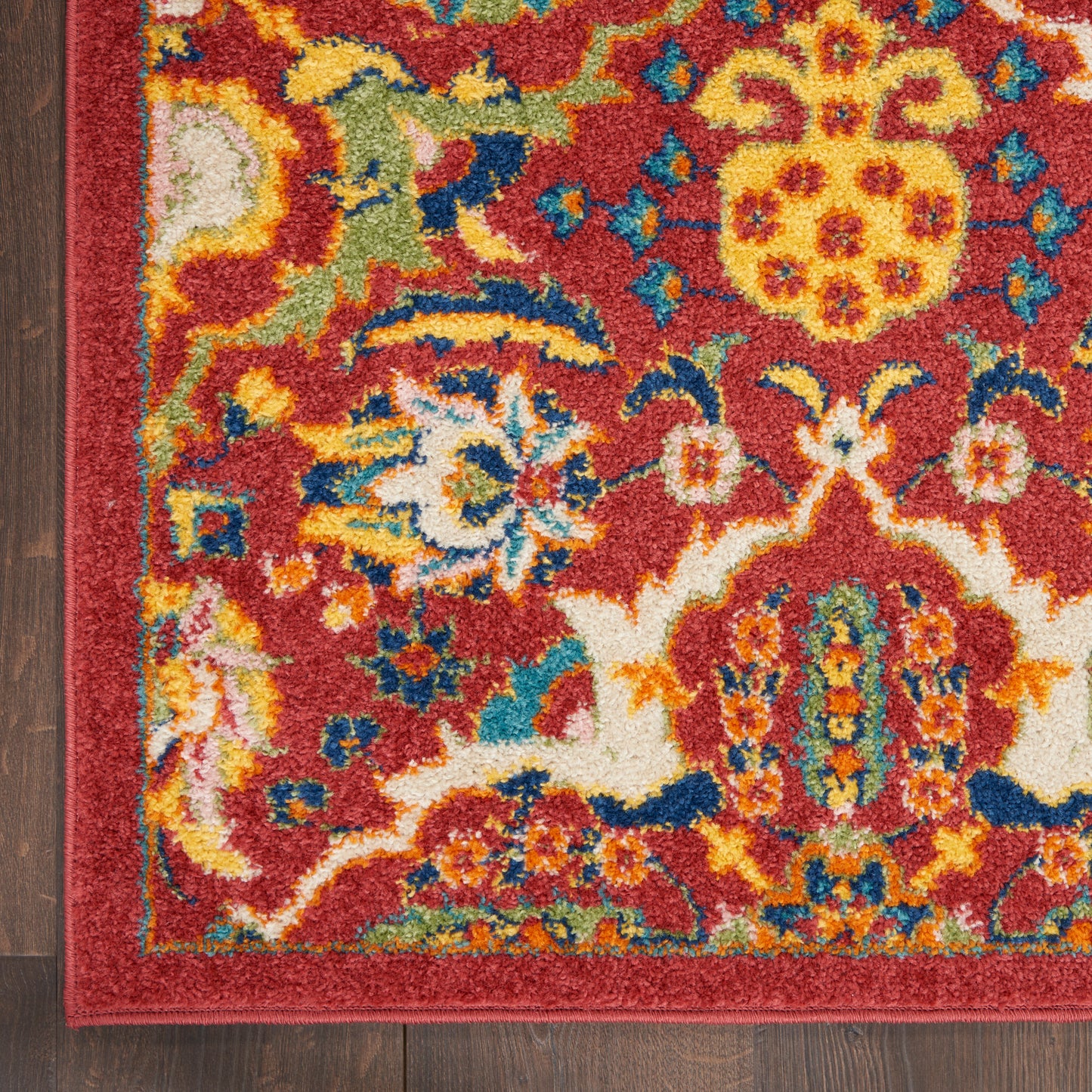 Close-up of a red bohemian-style rug with yellow, blue, green floral motifs and a matching border on dark wood floor.