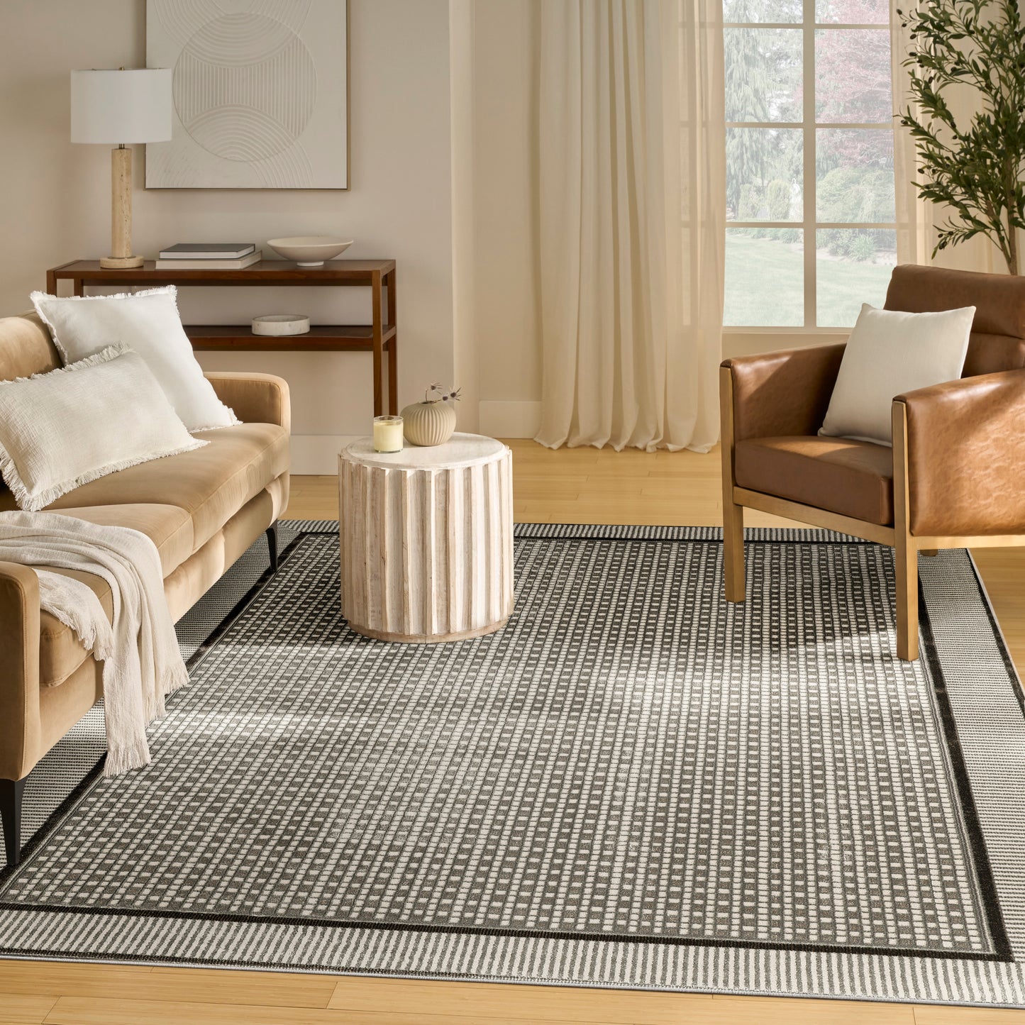 Neutral living room with beige sofa, brown leather armchair, round ribbed wood coffee table, striped rug, light curtains.