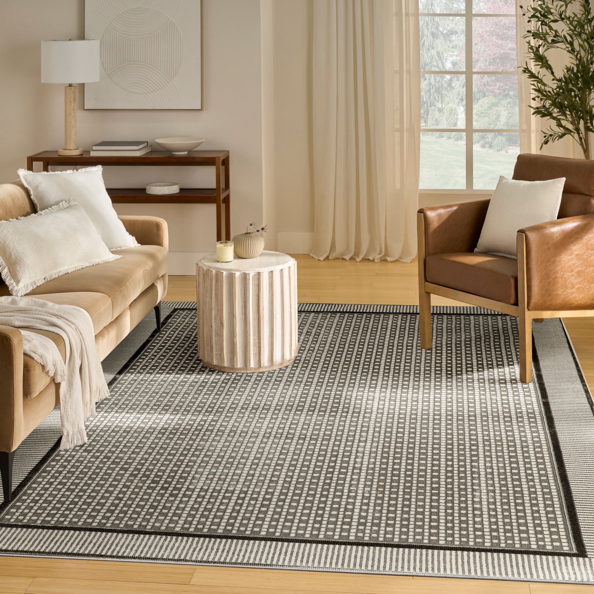 Neutral living room with beige sofa, brown leather armchair, round ribbed wood coffee table, striped rug, light curtains.