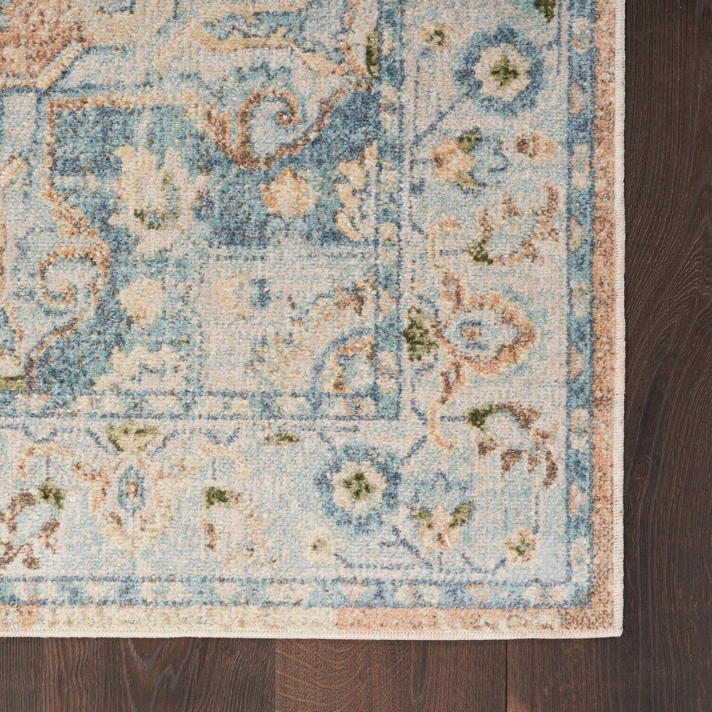 Rectangular distressed oriental area rug in blue, ivory and tan with floral border on dark wood floor.