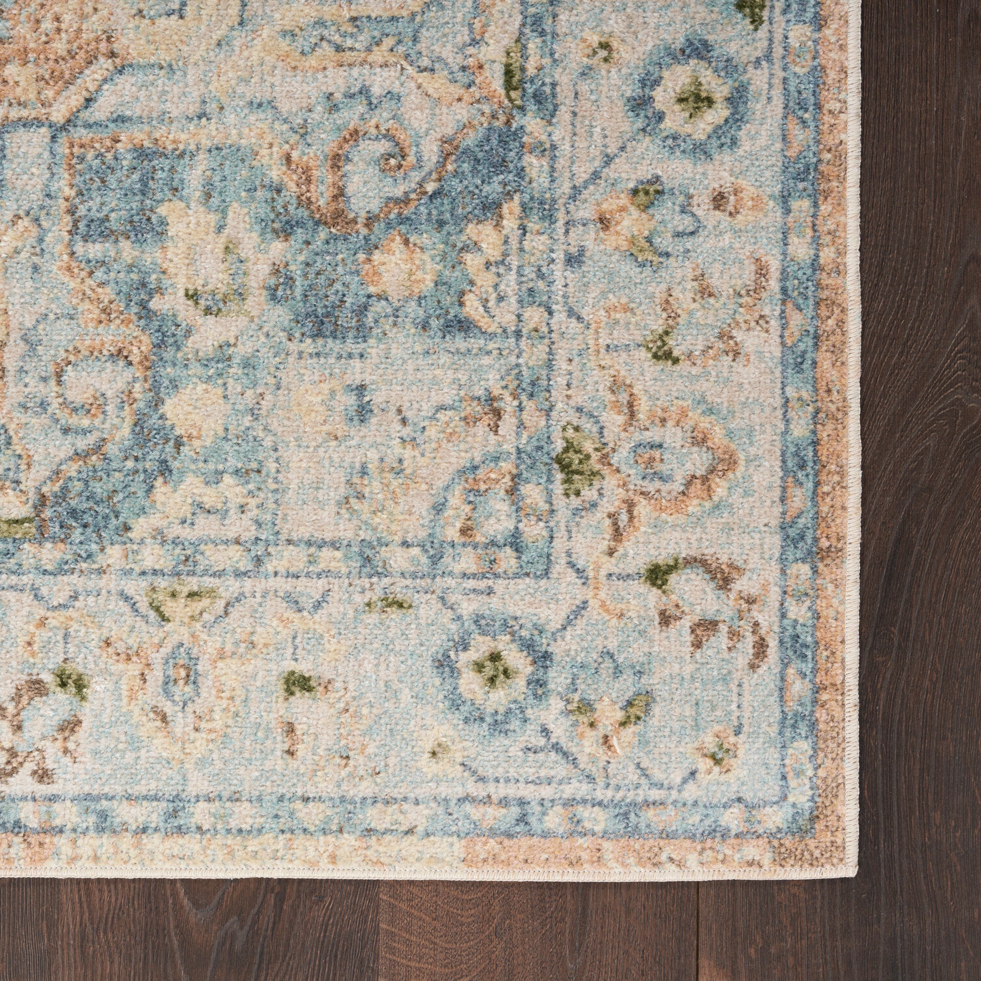 Rectangular distressed oriental area rug in blue, ivory and tan with floral border on dark wood floor.