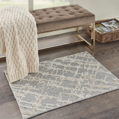 Taupe tufted bench with gold metal frame, cream knit throw, grey lattice rug, and wicker magazine rack on dark wood floor.