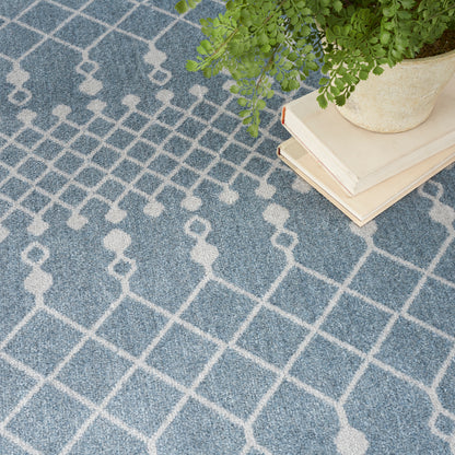Blue geometric rug with white lattice pattern; plant in pot atop beige books on corner.