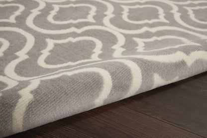 Soft gray and white geometric trellis rug with a woven texture on dark wood floor.