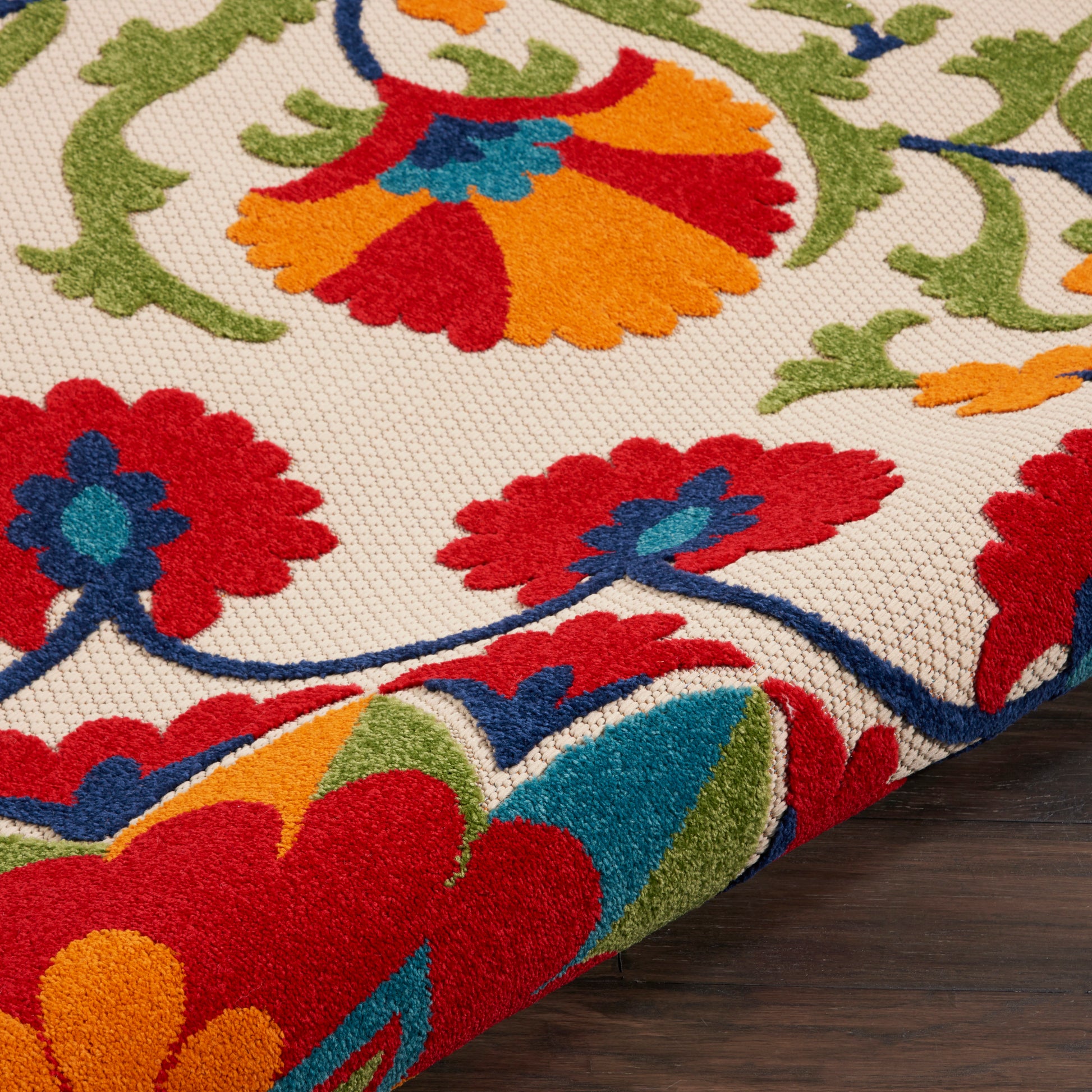 Vibrant floral rug with red, orange, blue and green petals on a beige background; thick pile edge curling.
