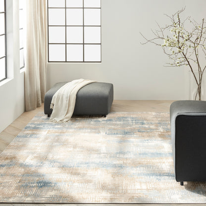 Abstract beige, cream and blue area rug on a light wood floor in a modern living room with gray ottomans and a cream throw.
