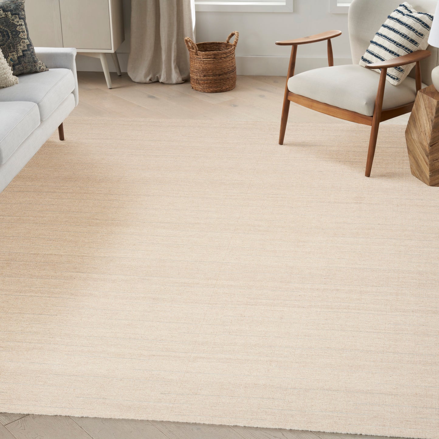 Light beige woven rug in a bright living room with a white sofa, mid-century wooden chair, and woven basket.