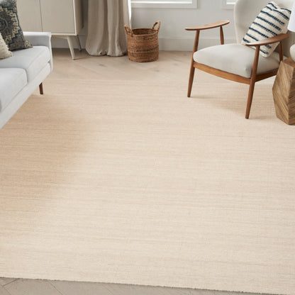 Light beige woven rug in a bright living room with a white sofa, mid-century wooden chair, and woven basket.