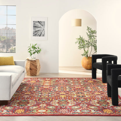 Vibrant oriental-style rug in red, yellow, blue on light wood floor; white sofa, black curved chairs, potted plants.