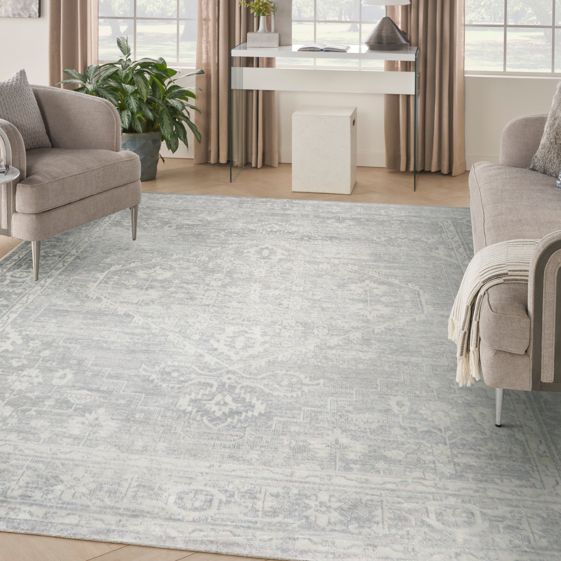 Pale blue-gray patterned rug anchors a beige living room with upholstered chairs, light wood floors, and a white console near windows.