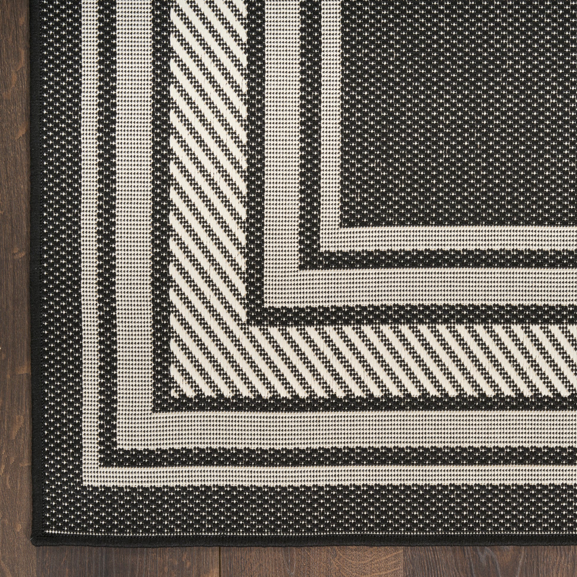 Black and ivory woven rug with nested rectangular borders and diagonal striped section on dark wood floor.