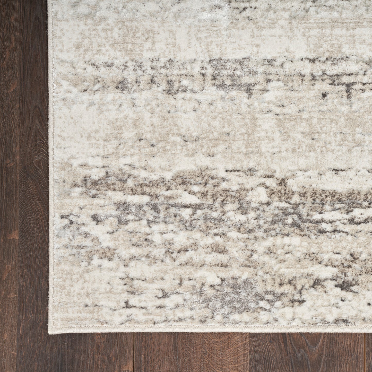 Beige-gray distressed abstract area rug on dark wood floor with a pale border.