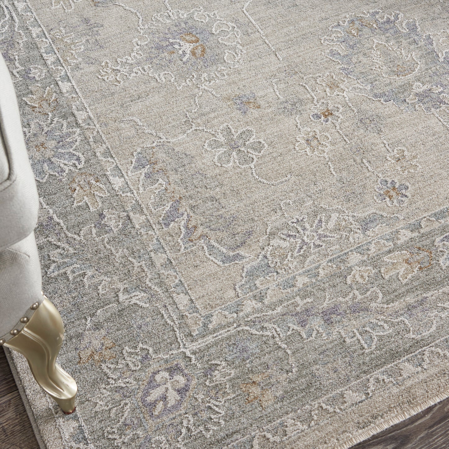 Light gray oriental area rug with blue floral motif & decorative border; beige chair leg with gold accent beside.