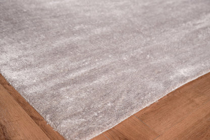 Light gray plush hand-knotted area rug on warm brown hardwood floor, edge visible.