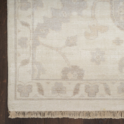 Cream flat-weave rug with subtle floral motif and fringe along the edge on a dark wood floor.