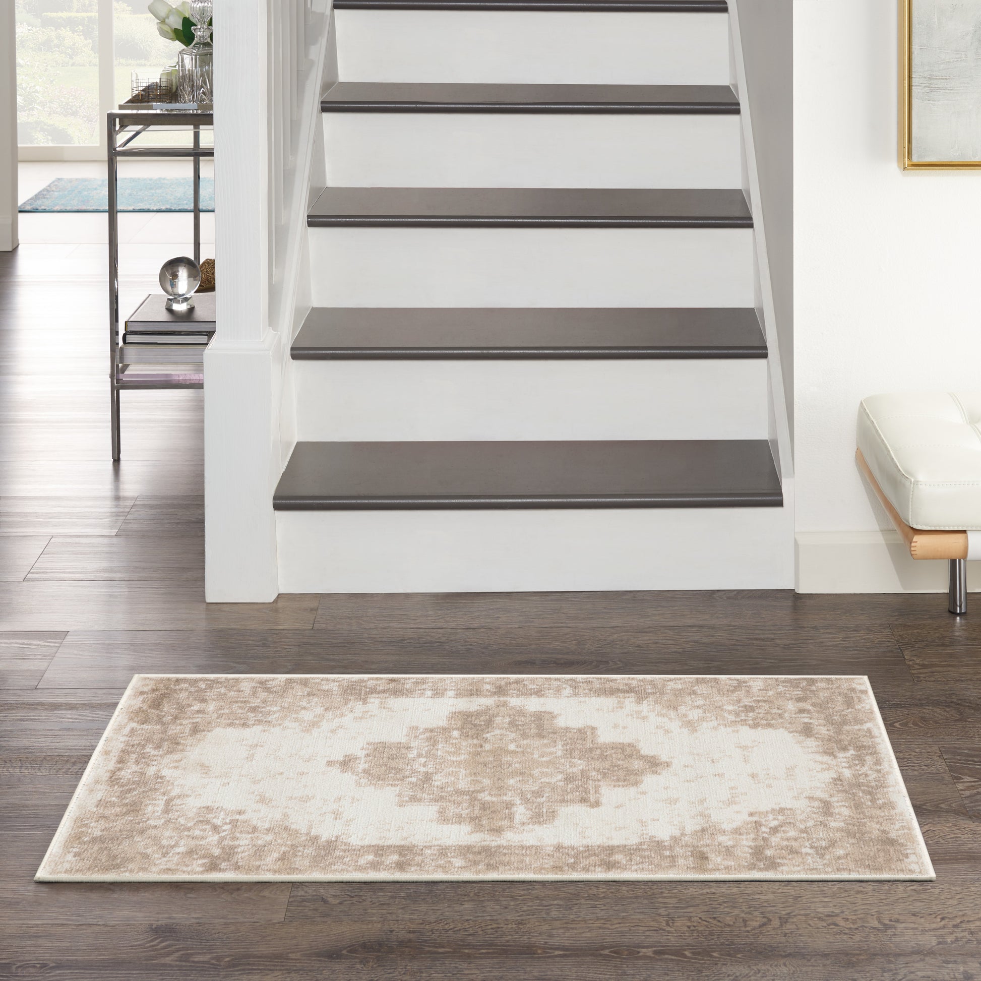 Beige and cream geometric rug on dark wood floor beside white staircase with dark treads; modern entry scene.