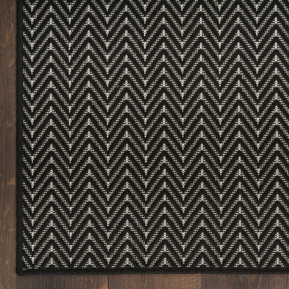 Rectangular black and white chevron rug with textured zigzag weave on wooden floor.