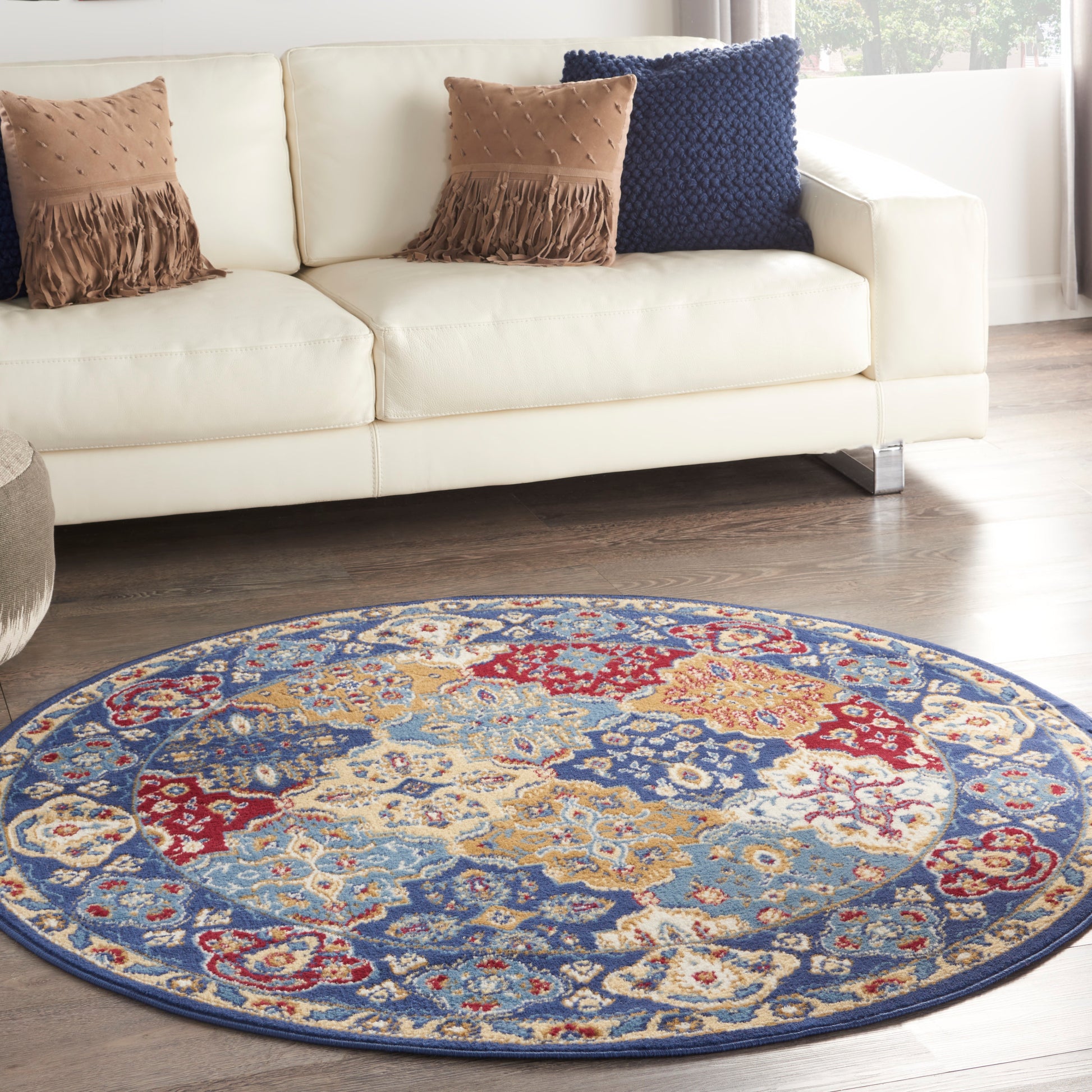 Round multicolor Persian-style rug on dark wood floor with a white sofa and brown fringe cushions