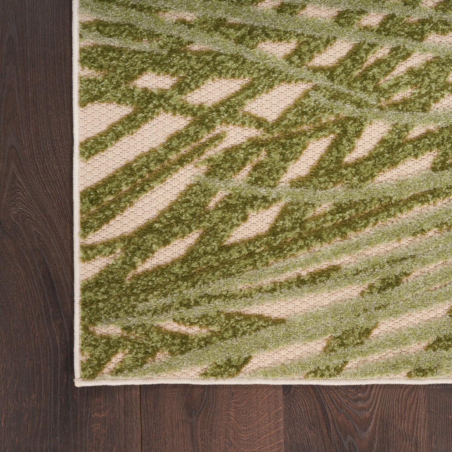 Green abstract-patterned rug with beige background, textured pile, cream border, on dark wood floor.