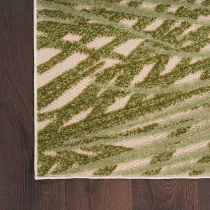 Green abstract-patterned rug with beige background, textured pile, cream border, on dark wood floor.