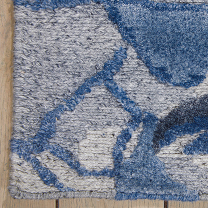 Blue and gray geometric rug with diamond shapes and loop pile on light hardwood floor.