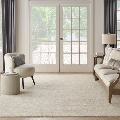 Neutral living room with beige rug, cream curved chair, beige tufted sofa, round concrete side table, wood accents & white French doors.