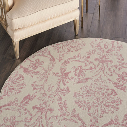 Round beige rug with pink damask floral pattern; paired with cream chair and dark wood floor.