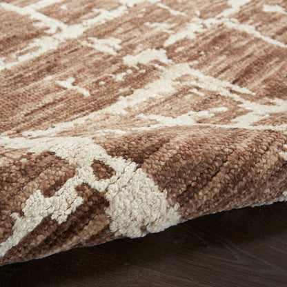 Brown and ivory geometric shag rug with plush pile, edge folded over on dark wood floor.