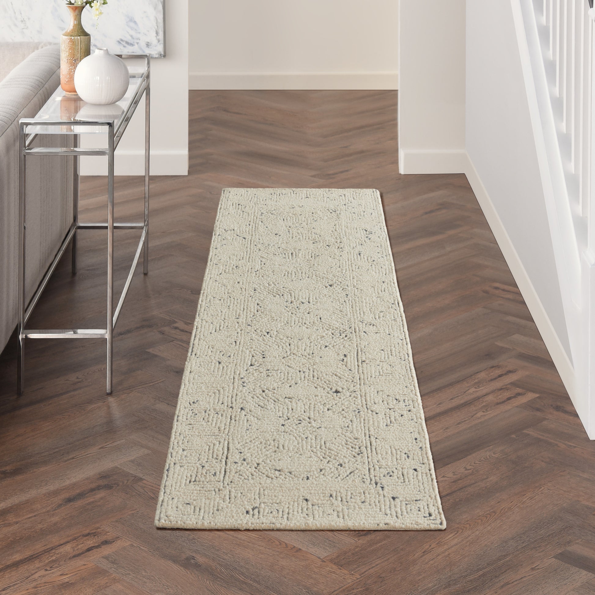Long beige textured runner rug on a dark herringbone hallway floor beside a glass-top metal console table.
