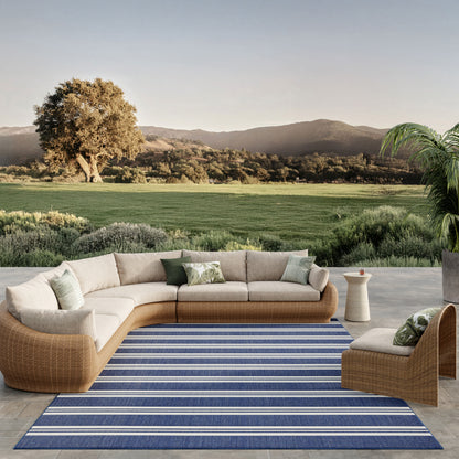 Modular outdoor rattan sectional with beige cushions on a blue striped rug, modern patio lounge.