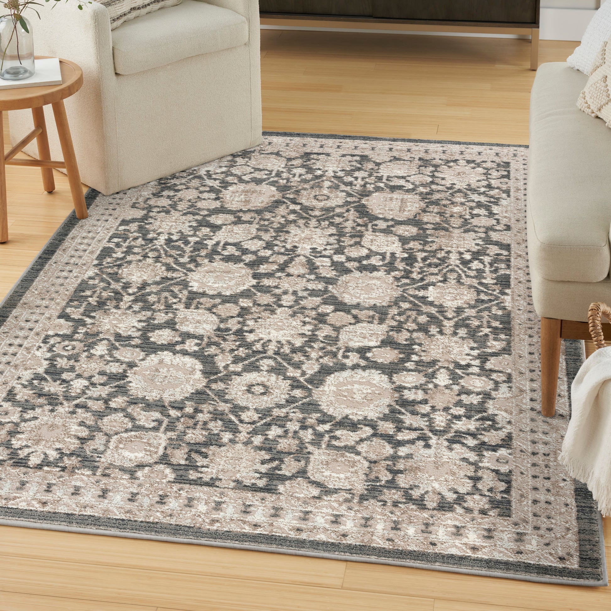 Oriental floral area rug in ivory and charcoal with a light border on light wood floor, beige sofa nearby.