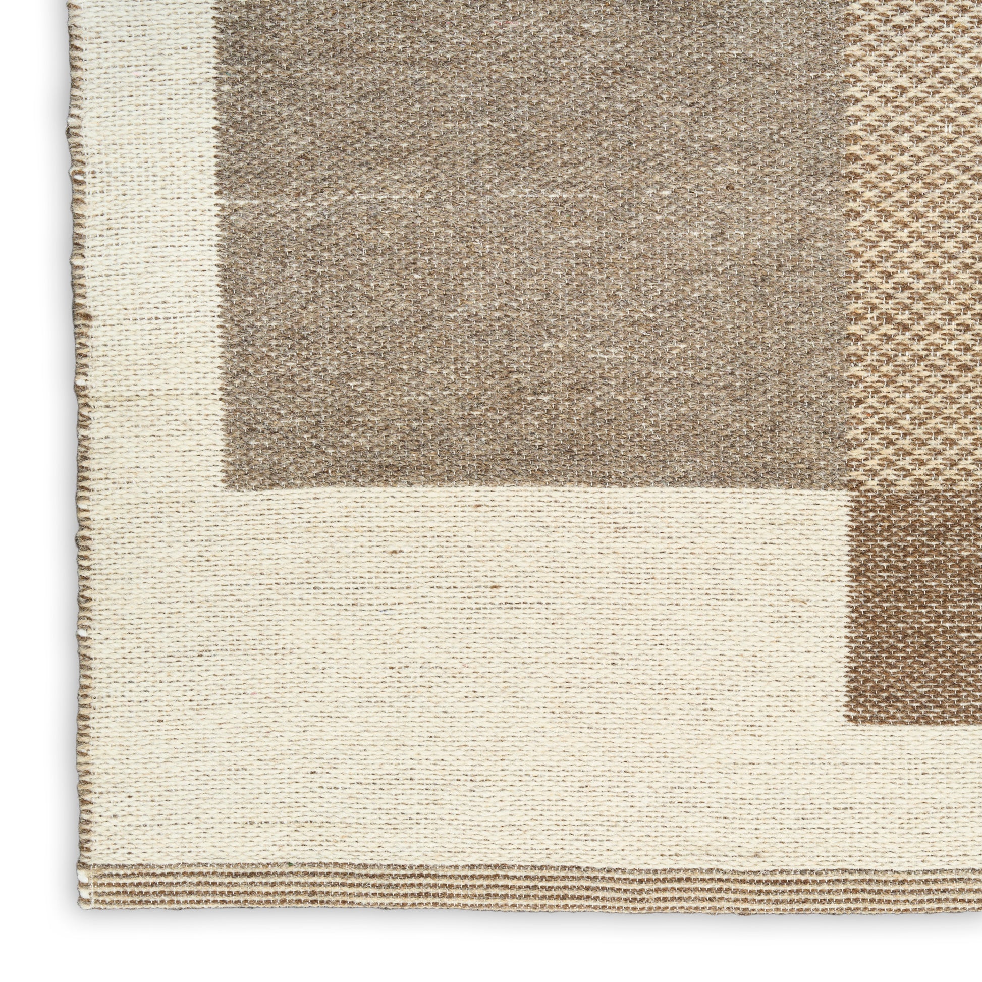 Close-up of a woven area rug corner with cream border and geometric taupe-beige blocks, natural textured fibers.