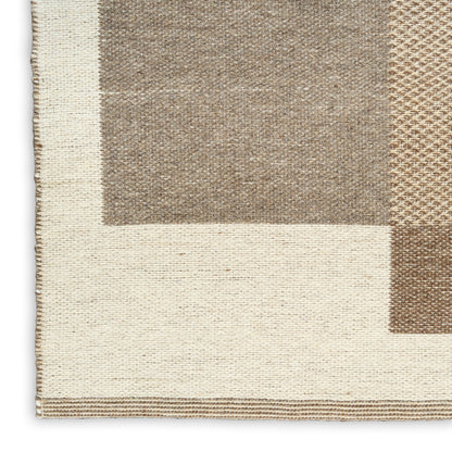 Close-up of a woven area rug corner with cream border and geometric taupe-beige blocks, natural textured fibers.