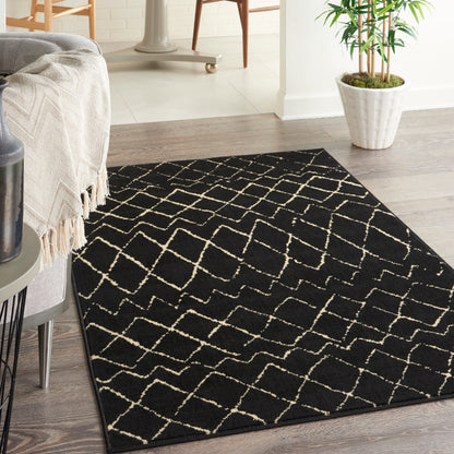 Black rug with cream geometric lattice pattern on wood floor, with beige fringed throw and potted plant
