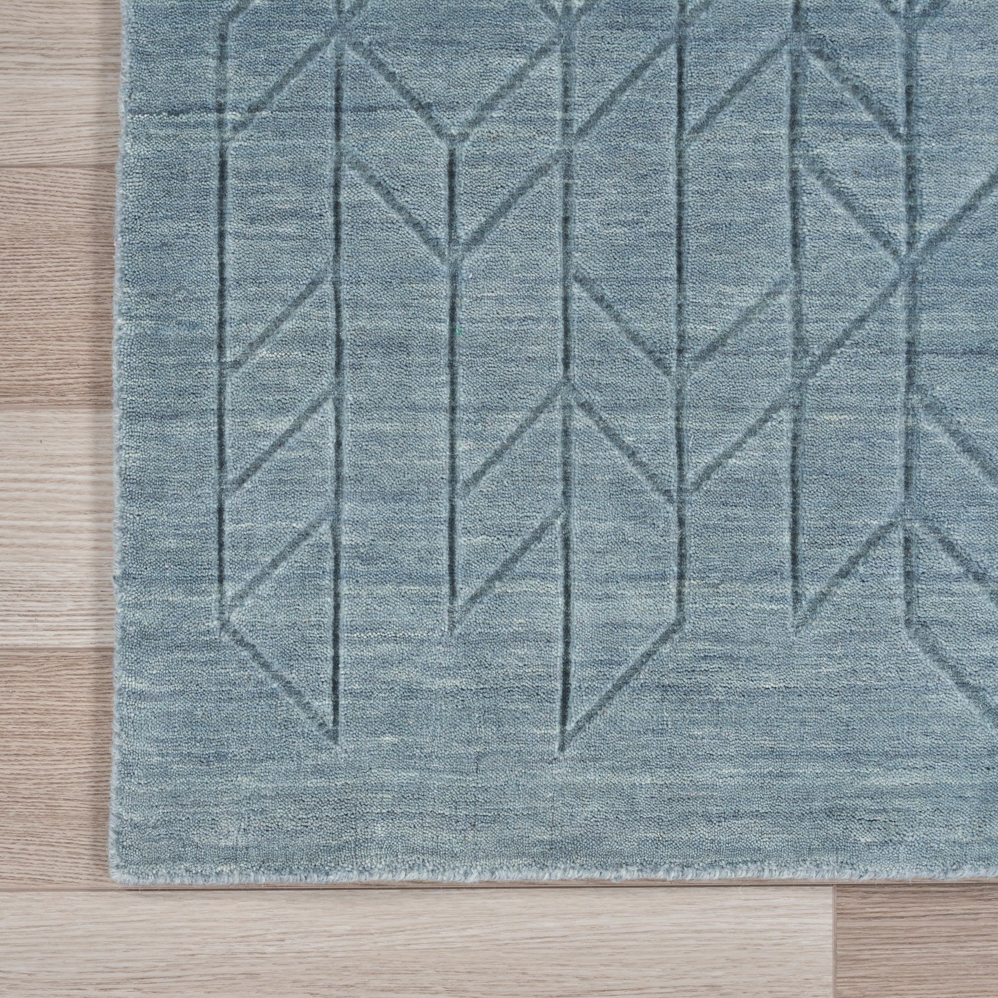 Blue-gray rug with a geometric chevron/diamond grid pattern on a wood floor.