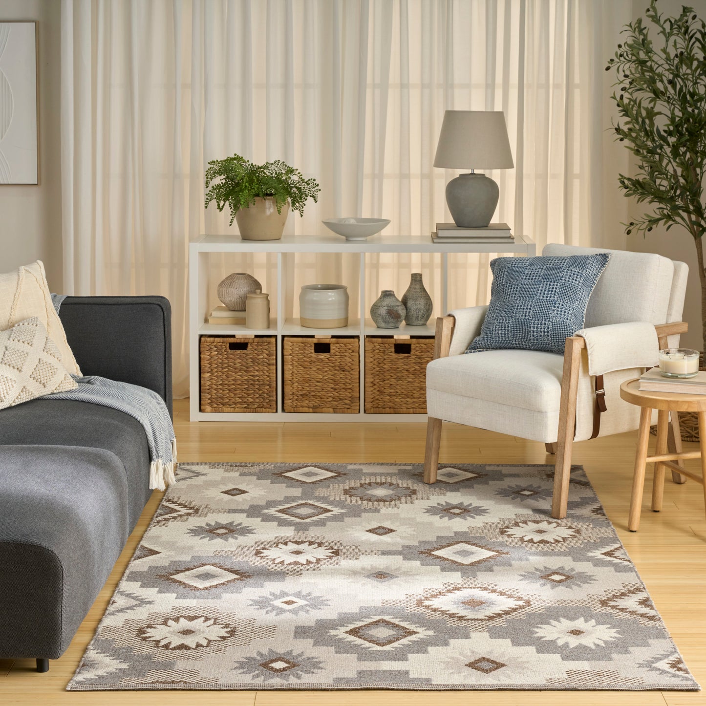 Cozy living room with a grey sofa, white shelf, woven baskets, an armchair with a blue cushion, a geometric rug and potted plants