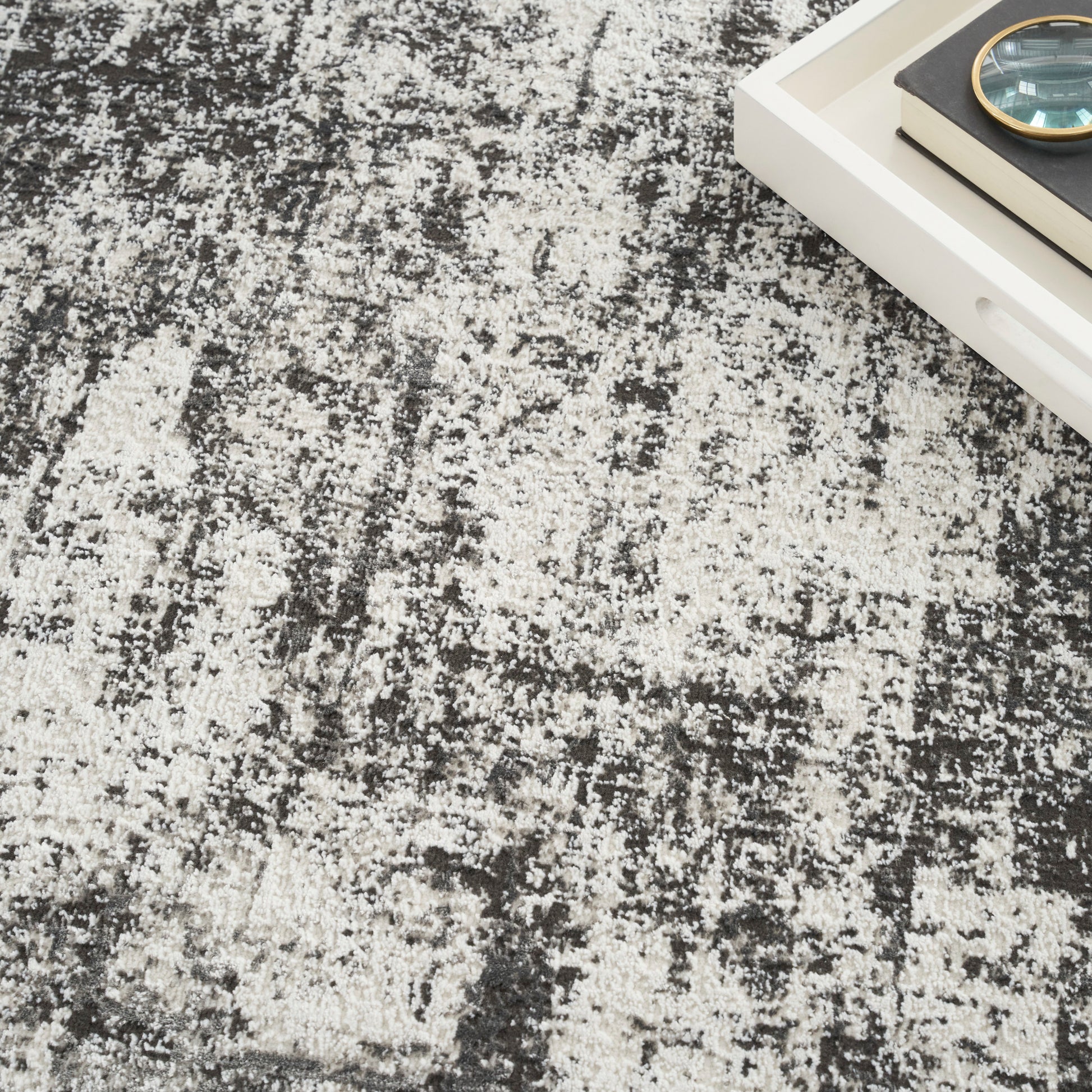 Modern distressed gray and white rug; white tray with book and magnifying glass sits on the corner.