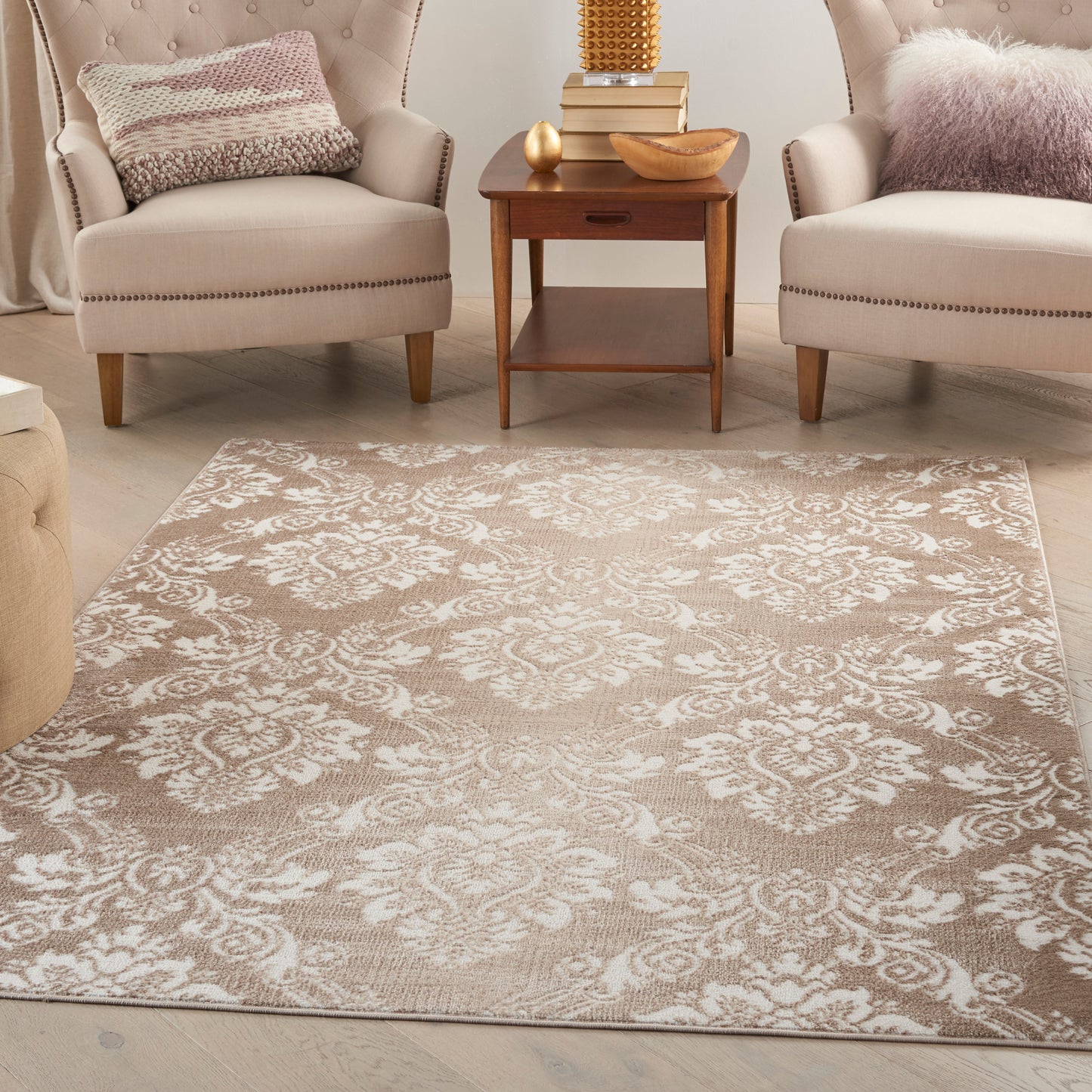 Beige floral damask area rug between two cream upholstered armchairs with nailhead trim & a wooden side table.