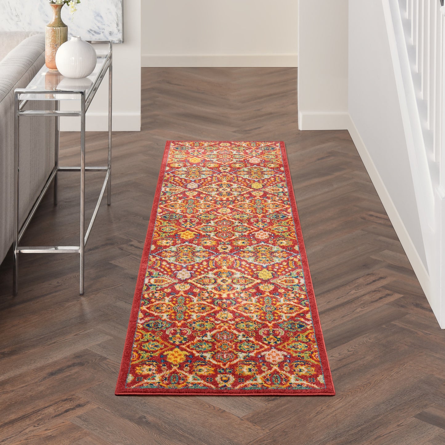 Long colorful geometric oriental rug runner with red border on dark wood floor in a hallway.