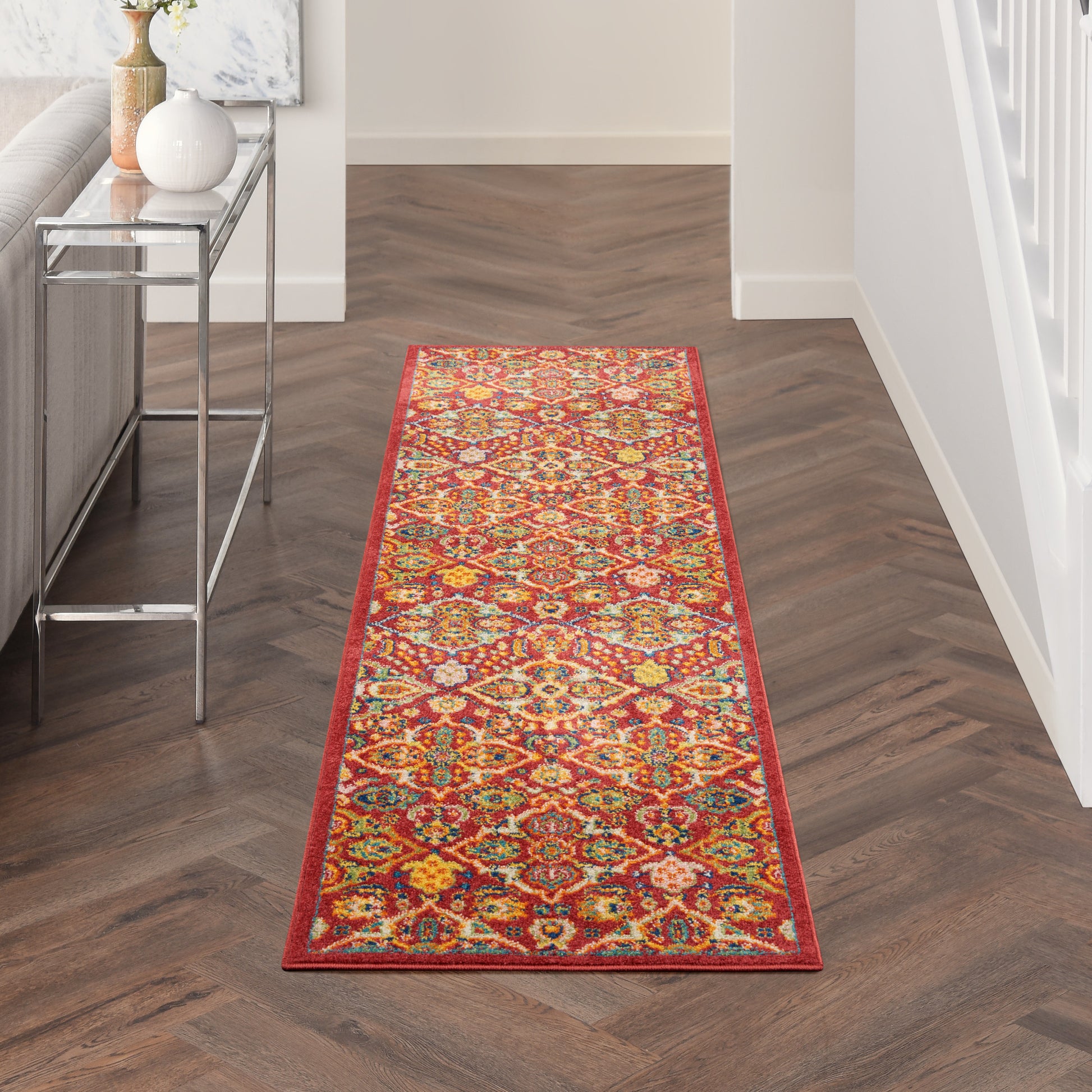 Long colorful geometric oriental rug runner with red border on dark wood floor in a hallway.