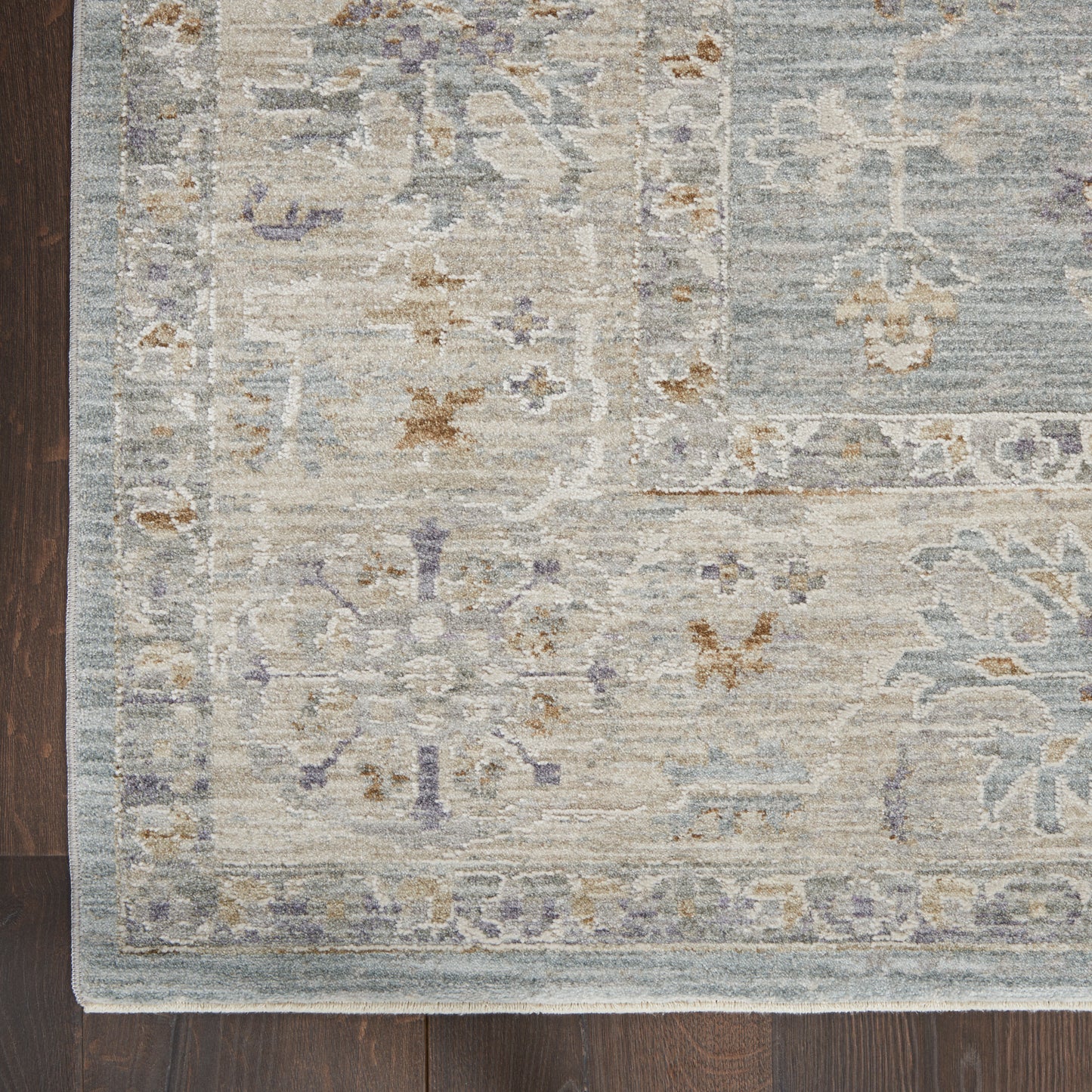 Distressed light blue & beige oriental rug with lavender floral motifs & pale border on dark hardwood floor