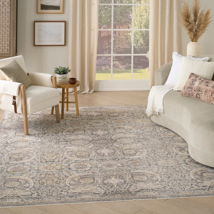 Neutral living room with a large gray-beige patterned rug, beige sofa, white chair, and wooden side table by a bright window.