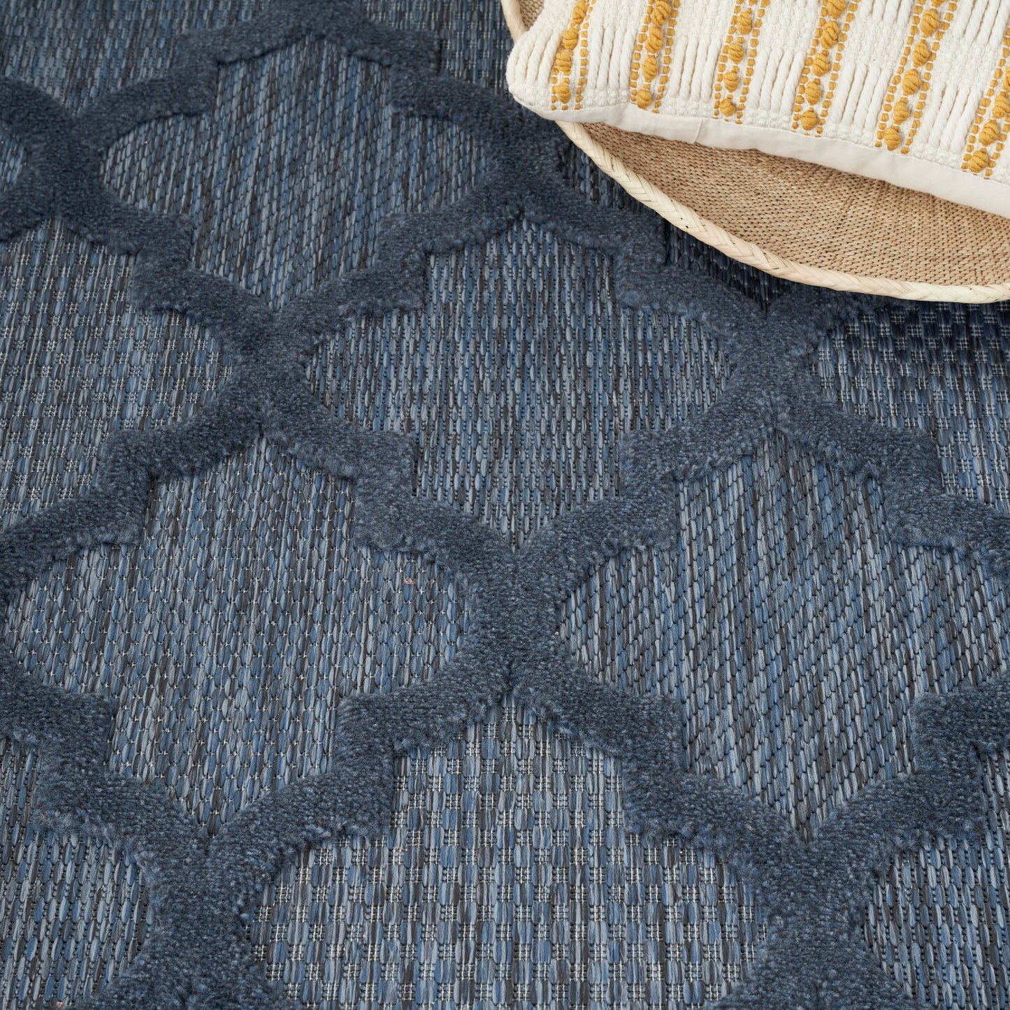 Blue woven rug with raised dark diamond lattice pattern; straw hat peeking in the corner.