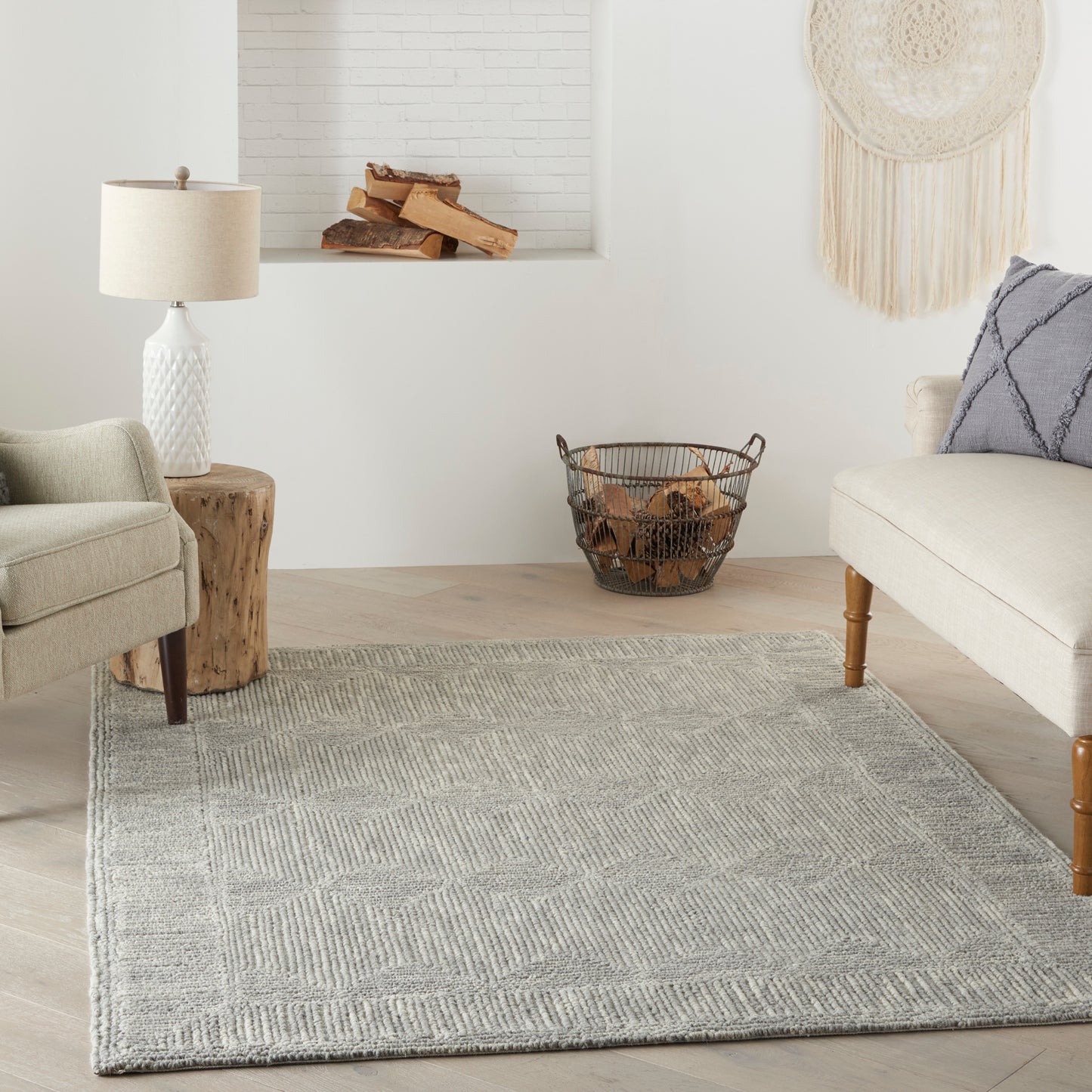 Neutral living room with light gray geometric rug, beige sofa, wood stump side table, lamp, and firewood basket.