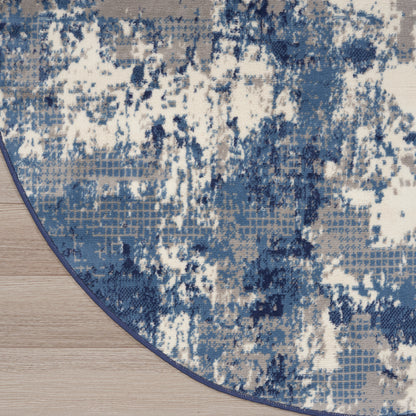 Round rug with blue, white and gray abstract distressed pattern on wood floor.