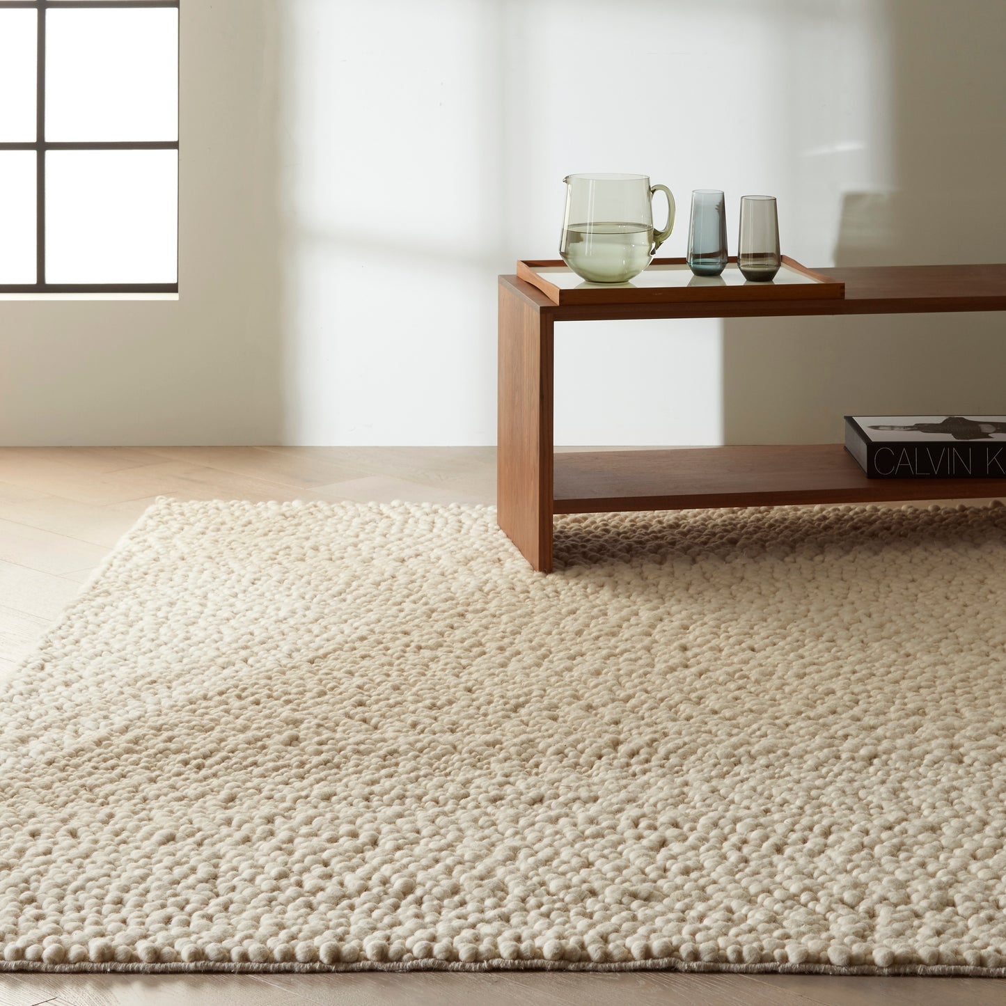 Beige textured rug with a tray holding a glass pitcher and two glasses, and a book nearby.